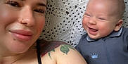 Ezra is registered to the contest to win money with this photo: woman, baby, smiling, tattoo, nose_ring, crocheted_blanket, blue_outfit, lying_down, happy, face, skin, person, portrait, indoor, closeup, head, expression, casual_clothing, parent, child