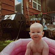 Clara is registered to the contest to win money with this photo: baby, infant, inflatable_pool, pink, backyard, grass, house, door, window, plants, potted_plants, compost_bin, outdoor, summer, child, smile, skin, bare_chest, daylight