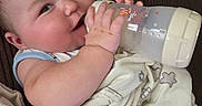 Levi is registered to the contest to win money with this photo: baby, infant, child, smiling, bottle, feeding, blanket, cushion, portrait, face, eyes, hands, sitting, cozy, indoor, close_up, happy, nursery, textile, caregiving