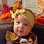 baby, headband, bow, autumn_leaves, wicker_chair, closeup, cute, child, portrait, seasonal, orange, red, yellow, face, infant, decor, expression, seated, indoors, soft_light