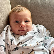 Simon a rejoint le concours — aidez-le/la à gagner de superbes lots ! baby, infant, couch, sweatshirt, dinosaur_print, smile, face, child, indoors, cozy, cute, clothing, person, seated, portrait, young_child, fabric, texture, beige, happy