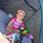 Idyle a rejoint le concours — aidez-le/la à gagner de superbes lots ! baby, child, tent, toy, pink_clothing, cap, ball, plush_toy, small_car, colorful, smiling, sitting, indoors, playtime, cute, happy, infant, soft_light, fabric, fun