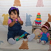 Nazneen joined the competition — help win amazing prizes! toddler, child, denim_overalls, purple_headband, clapping, blanket, bunny_patterns, toy_microphone, wooden_crate, stacking_rings, doll, colorful_toy, pink_shirt, white_sneakers, indoor, happy, sitting, playtime, cute, portrait