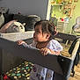 Nazneen joined the competition — help win amazing prizes! toddler, child, playpen, indoors, living_room, curious, hair_clip, white_dress, cushion, sofa, kitchen, shelf, jar, high_chair, floor, wood_floor, bracelet, person, furniture, baby