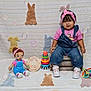 Nazneen joined the competition — help win amazing prizes! baby, child, denim_overalls, pink_headband, pink_shirt, white_sneakers, toy_doll, stacking_rings, wooden_crate, plush_bunnies, blanket, bubbles, milestone_sign, indoor, cute, smiling, sitting, colorful, playful, portrait