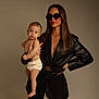 child, baby, infant, woman, adult, sunglasses, leather_jacket, belt, gucci_belt, portrait, studio, neutral_background, posing, holding, parent_child, bare_skin, diaper, fashion, jewelry, long_hair
