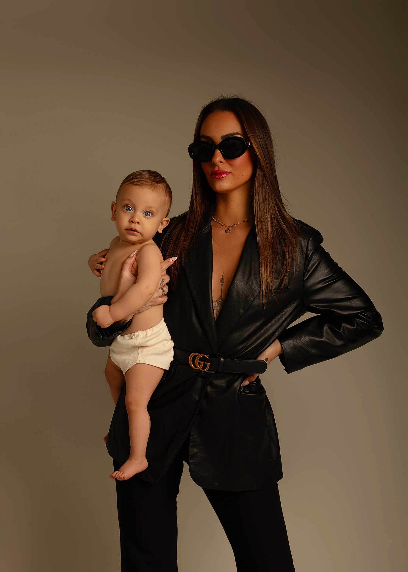 Alessio participe au concours pour gagner de l'argent avec cette photo : child, baby, infant, woman, adult, sunglasses, leather_jacket, belt, gucci_belt, portrait, studio, neutral_background, posing, holding, parent_child, bare_skin, diaper, fashion, jewelry, long_hair