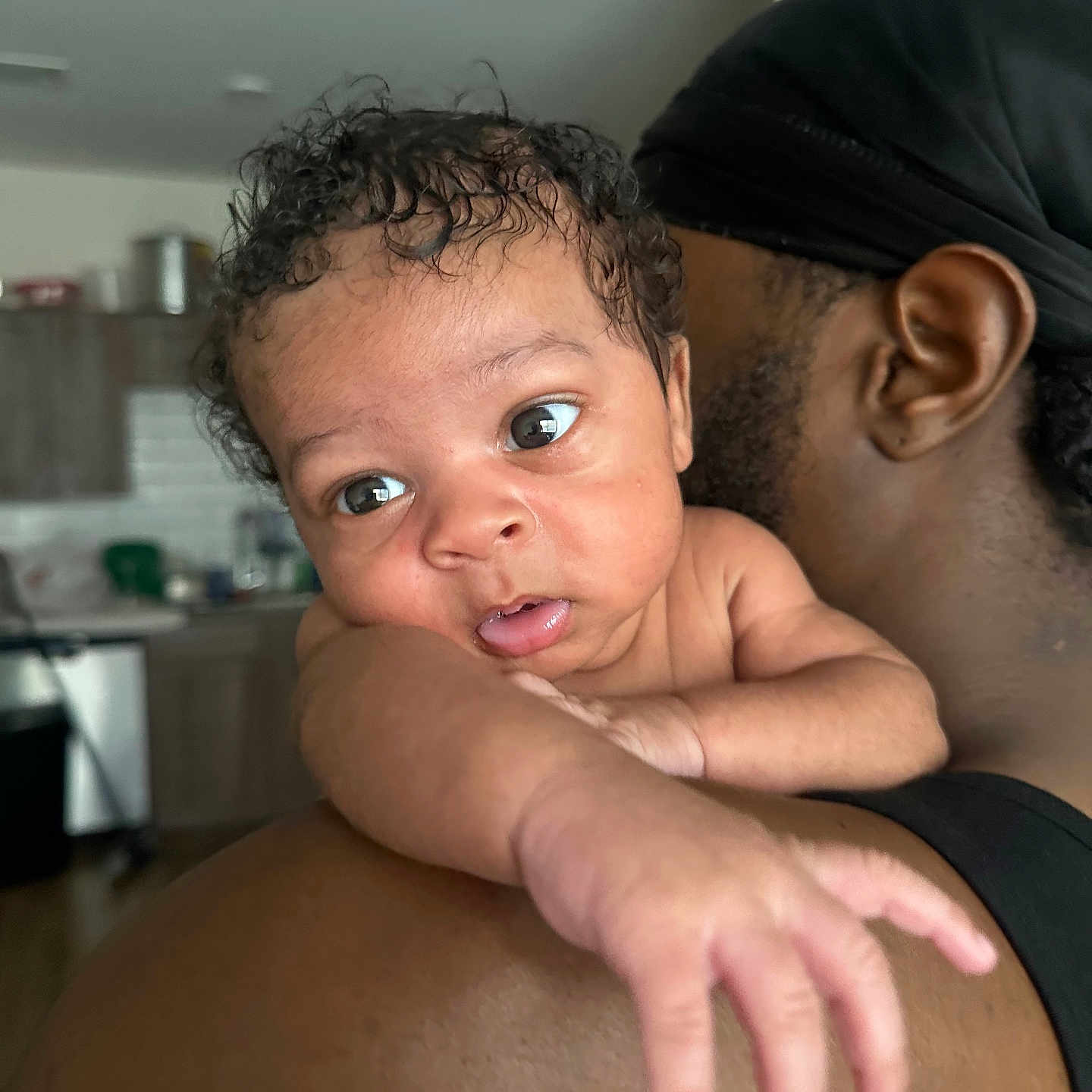 Apharri joined the competition — help win amazing prizes! baby, infant, child, person, arm, shoulder, skin, curly_hair, indoor, adult, headwear, black_clothing, expression, reaching, closeup, face, portrait, room, background, holding