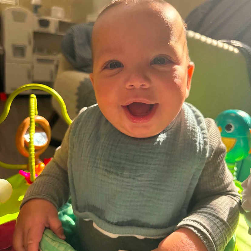 Auziel is registered to the contest to win money with this photo: activity_center, baby, bib, child, clothing, colorful, cute, face, hand, happy, indoor, infant, person, play, portrait, smiling, sunlight, toy, warm_light, young
