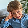 child, boy, smile, blue_shirt, couch, indoor, portrait, happy, casual, face, young, person, blond_hair, button_up, relaxed, home, furniture, plant, background_blur, cheerful