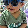 Sultan joined the competition — help win amazing prizes! toddler, child, sunglasses, green_tshirt, smiling, indoor, hand_holding, short_hair, bed, purple_bedspread, camouflage_shorts, person, face, playful, happy, casual_clothing, young_child, home, cute, portrait