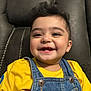 Sultan is registered to the contest to win money with this photo: toddler, child, smile, happy, denim_overalls, yellow_shirt, baby, face, portrait, indoor, couch, furniture, cute, young_child, person, skin, hair, sitting, closeup, expression