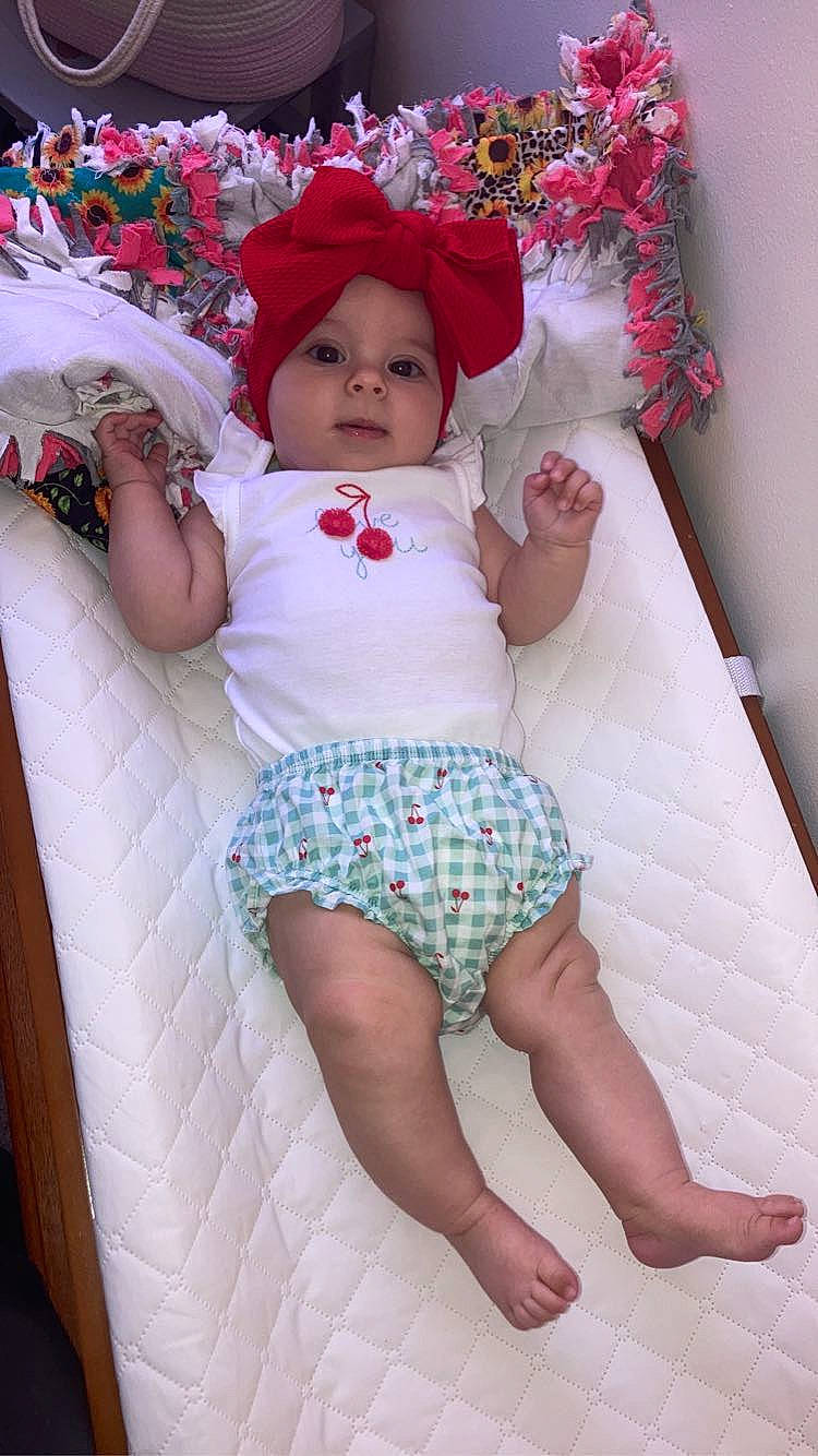 Sophia is registered to the contest to win money with this photo: arm, baby, baby_toddler_clothing, child, comfort, eye, face, finger, headwear, human_body, knee, lap, leg, organ, person, pink, skin, stomach, textile, thigh