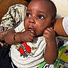 Milo joined the competition — help win amazing prizes! baby, infant, child, person, hand, fist, clothing, tshirt, bracelet, jewelry, sitting, lap, indoor, wooden_floor, tattoo, curious, big_eyes, cute, casual, portrait