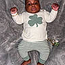 Milo is registered to the contest to win money with this photo: baby, infant, child, sweater, pants, striped_clothing, bracelet, blanket, dinosaur_pattern, lying_down, raised_arms, cute, portrait, indoor, footwearless, accessory, green, white, expression, person