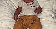Milo is registered to the contest to win money with this photo: baby, child, smile, nike, shoes, brown_shorts, white_cushion, jewelry, bracelet, necklace, tshirt, happy, indoors, portrait, cute, sitting, footwear, fashion, infant, person