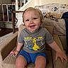 toddler, child, smiling, sitting, armchair, clothing, shorts, tshirt, indoor, living_room, furniture, staircase, blanket, happy, person, face, hair, carpet, home, cute
