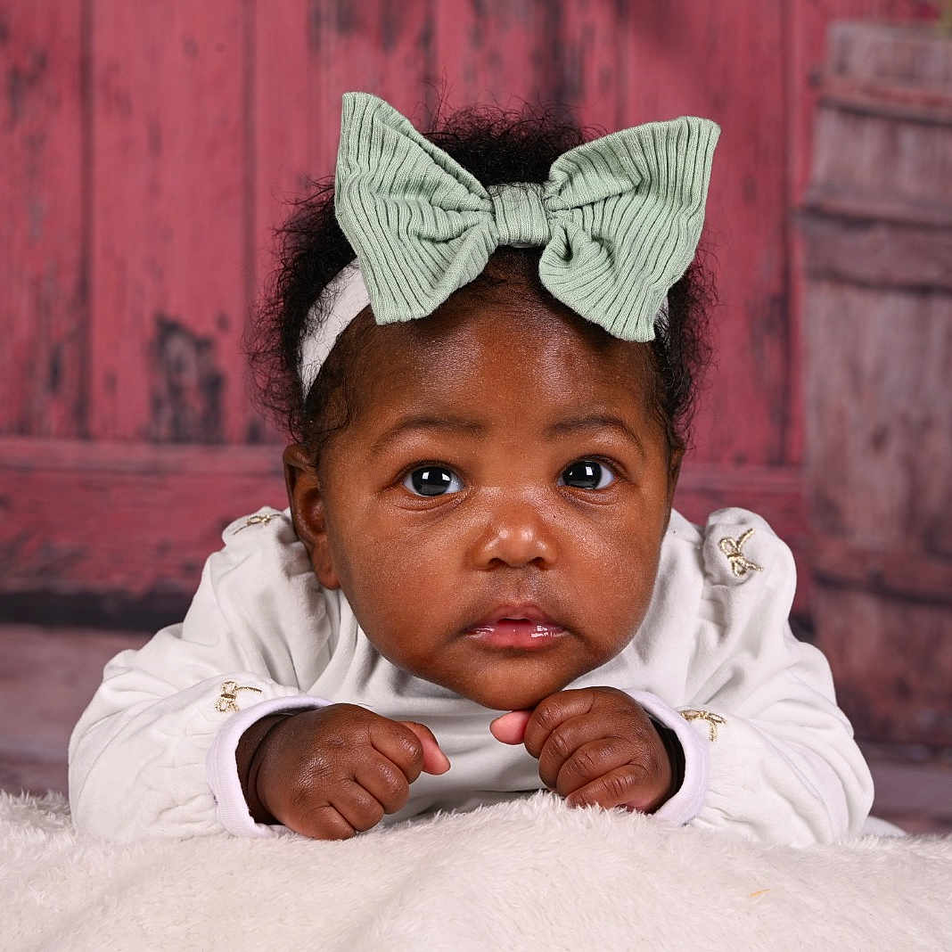 Kaylee a rejoint le concours — aidez-le/la à gagner de superbes lots ! baby, infant, child, headband, bow, white_clothing, curly_hair, fluffy_surface, red_background, wooden_wall, portrait, cute, hands, face, eyes, indoor, studio, skin, expression, closeup