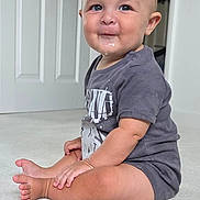 Jake is registered to the contest to win money with this photo: baby, child, sitting, carpet, indoors, tshirt, drool, smile, face, cute, young, person, skin, floor, room, door, short_hair, casual_clothing, expression, portrait