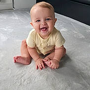 Jake is registered to the contest to win money with this photo: baby, carpet, child, clothing, cute, face, floor, furniture, hand, happy, indoor, infant, modern, person, short_sleeve, sitting, skin, smiling, toe, young