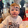 toddler, child, face_paint, bat, indoor, table, coloring_sheets, marker, white_sweatshirt, people, event, backpack, chair, window, curtains, wooden_floor, casual_clothing, portrait, expression, holiday