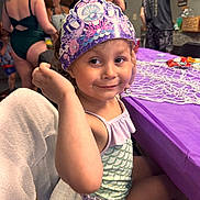Stella joined the competition — help win amazing prizes! adult, background, celebration, child, clothing, crown, face, fun, girl, hair, happy, indoor, party, people, pose, purple, skin, smile, swimsuit, table