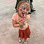 Stella is registered to the contest to win money with this photo: child, colorful, concrete_floor, cute, event, face_paint, fun, girl, happy, indoor, joy, lollipop, people_in_background, person, playful, skirt, smiling, sneakers, standing, tshirt
