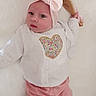 baby, bow, child, clothing, cute, expression, face, footwear, headband, heart_design, indoor, infant, lying_down, pink_clothing, portrait, ribbon, small_hands, soft_surface, white_sweater, wooden_hairbrush