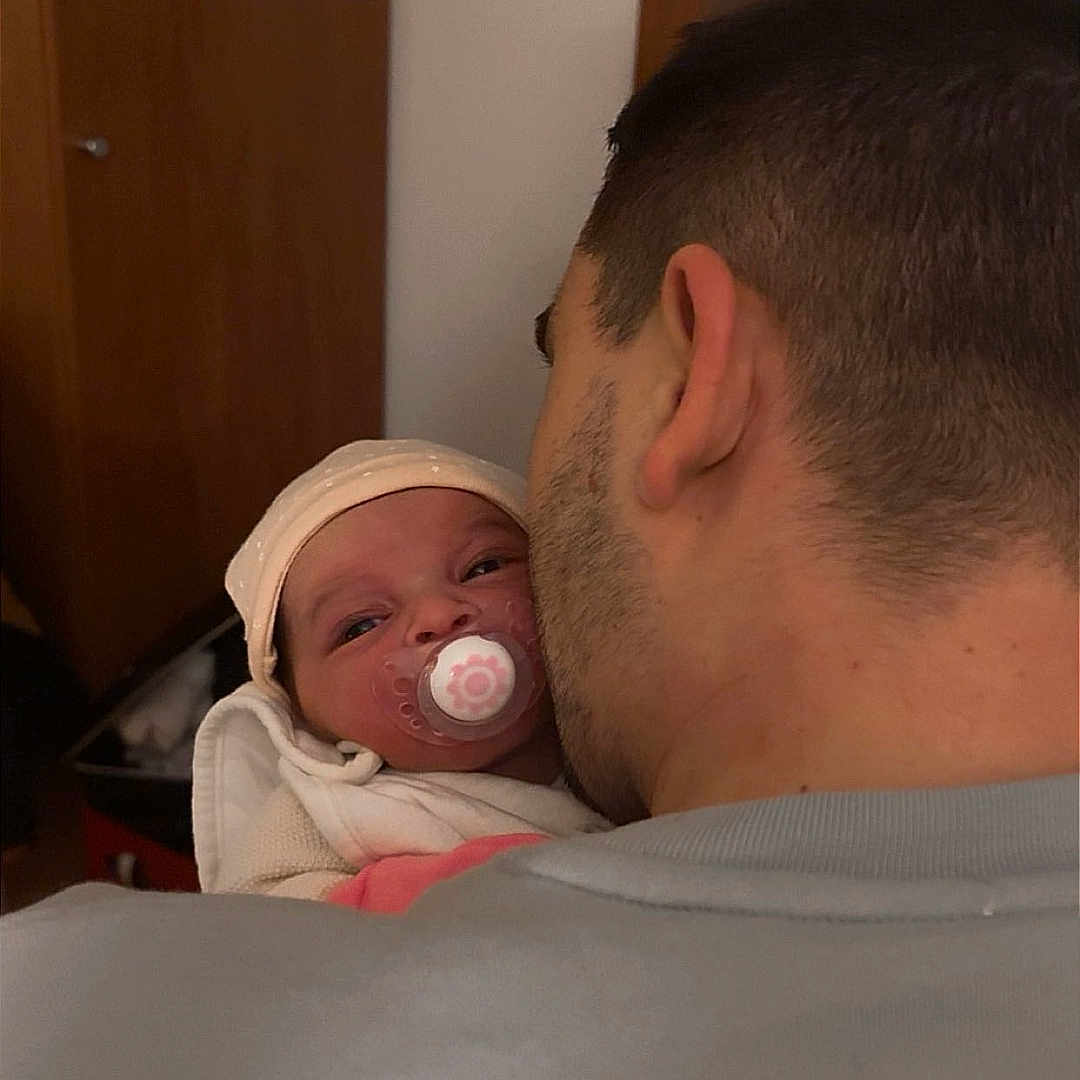 Lyana a rejoint le concours — aidez-le/la à gagner de superbes lots ! adult, baby, back_of_head, blanket, close_up, clothing, ear, furniture, hat, holding, indoor, man, newborn, pacifier, parenting, portrait, stubble, swaddle, warm_lighting, wooden_door