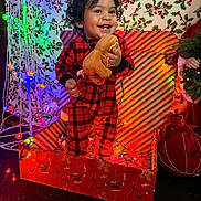 Kai is registered to the contest to win money with this photo: celebration, child, christmas, christmas_lights, curly_hair, decorations, festive, gift_box, gingerbread_man, happy, holiday_decor, holly_wallpaper, indoors, joy, person, plush_toy, red_pajamas, smiling, striped_wrapping_paper, toddler