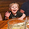 black_shirt, child, cute, dining, family, food, glass, happy, indoor, person, plate, restaurant, short_hair, smiling, table, toddler, water, waving, wooden_table, young_child