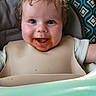 Ronin is registered to the contest to win money with this photo: baby, child, infant, high_chair, bib, smiling, happy, face, portrait, blue_eyes, curly_hair, brown_hair, baby_food, messy_face, eating, seated, indoor, patterned_background, close_up, photograph