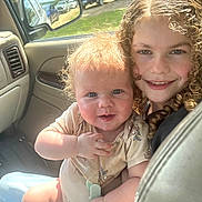 Ronin is registered to the contest to win money with this photo: children, baby, toddler, sibling, girl, curly_hair, smiling, portrait, car, vehicle, car_interior, seatbelt, sunlight, outdoor, parked_cars, window, family, infant, happy, selfie