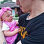 baby, man, tattoo, pink_headband, pink_dress, outdoor, house, greenery, holding, face, expression, curious, arm, short_sleeve, person, portrait, child, casual_clothing, daylight, closeup