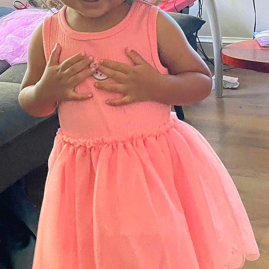Veronica joined the competition — help win amazing prizes! child, girl, pink_dress, sandals, indoor, living_room, television, table, floor, hair, ponytails, smiling, furniture, wooden_floor, toy, curtains, casual_clothing, person, standing, home