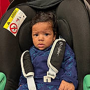 Djalil participe au concours pour gagner de l'argent avec cette photo : baby, black, blue_clothing, car_seat, car_seat_cushion, child, cute, expression, face, hair, indoor, infant, infant_clothing, levis, person, safety, seatbelt, sitting, straps, young_child