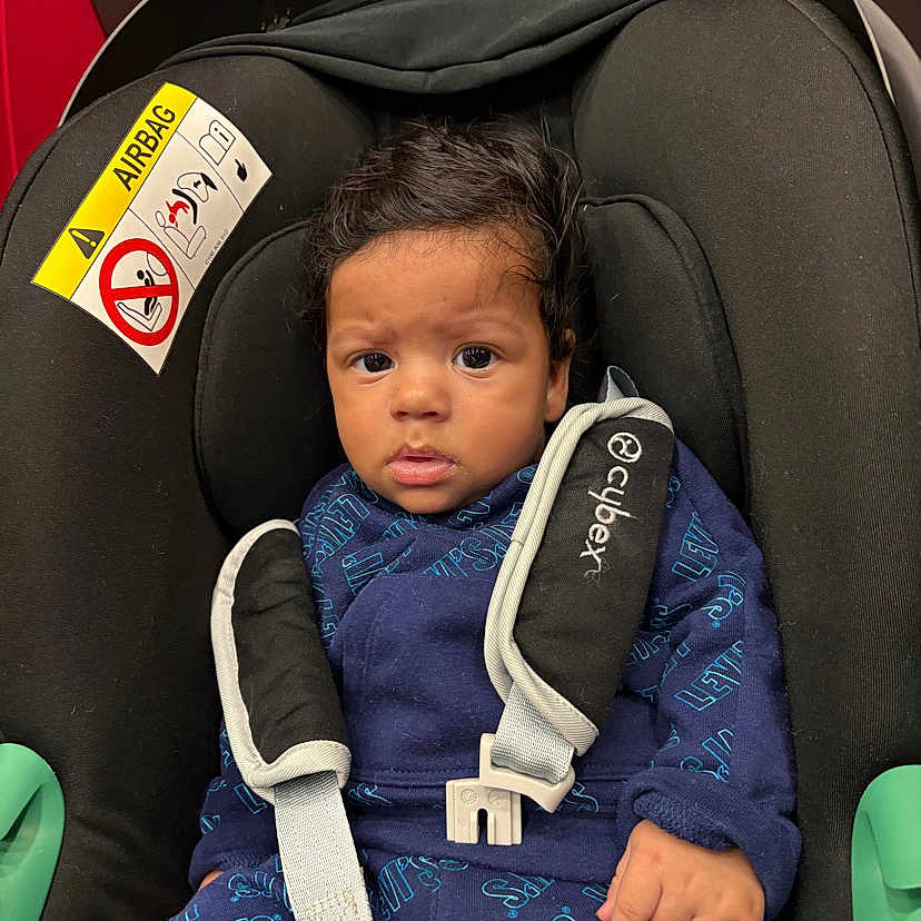 Djalil participe au concours pour gagner de l'argent avec cette photo : baby, black, blue_clothing, car_seat, car_seat_cushion, child, cute, expression, face, hair, indoor, infant, infant_clothing, levis, person, safety, seatbelt, sitting, straps, young_child