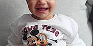 Kaira is registered to the contest to win money with this photo: toddler, child, smiling, sweatshirt, hat, pom_poms, mickey_mouse, pluto, couch, beige_pants, happy, indoor, portrait, cute, clothing, face, baby, sitting, cozy, casual
