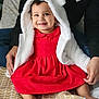 baby, child, smiling, red_dress, white_jacket, hood, bear_ears, sitting, bed, patterned_bedspread, happy, person, hands, indoor, cute, portrait, clothing, feet, young_child, childhood