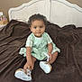 Malika participe au concours pour gagner de l'argent avec cette photo : baby, child, toddler, curly_hair, green_dress, shoes, bed, blanket, brown_blanket, headboard, indoor, portrait, smiling, sitting, furniture, person, cute, soft_lighting, looking_at_camera, home