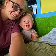 Beau is registered to the contest to win money with this photo: baby, child, adult, smiling, portrait, selfie, indoors, cafe, colorful_background, eyeglasses, crayon, worksheet, maze, menu, table, seated, happy, family, blonde_hair, closeup