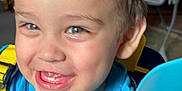 Ronnie is registered to the contest to win money with this photo: toddler, child, smiling, happy, face, blue_shirt, yellow_straps, blanket, knitted, indoor, home, person, young_child, closeup, portrait, cute, baby, hair, eyes, mouth