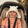 baby, bear_ears, black_straps, car_seat, cardboard_box, child, cute, hat, headwear, indoors, infant, person, pink_clothing, seat_belt, sitting, smile, soft_fabric, tiled_floor, white_hat, young_child