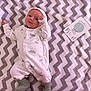 baby, infant, onesie, blanket, zigzag_pattern, milestone_card, smile, face, hand, feet, clothing, soft_toy_pattern, laying_down, cozy, cute, newborn, child, happy, milestone, indoor