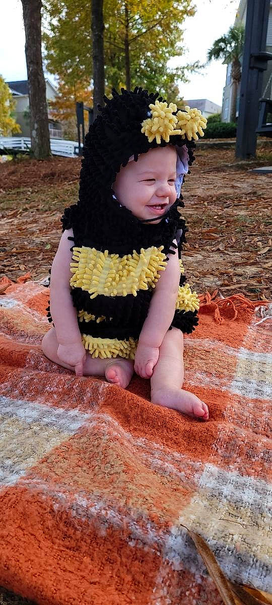 Greyson is registered to the contest to win money with this photo: baby_toddler_clothing, child, flower, fun, grass, happy, headband, headpiece, headwear, human_leg, jewellery, leaf, people_in_nature, person, photograph, pink, plant, sitting, soil, toddler