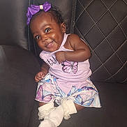 Jakerya is registered to the contest to win money with this photo: baby, child, smiling, purple_bow, butterfly, dress, socks, couch, leather, quilted, happy, cute, infant, portrait, indoor, person, seated, clothing, face, skin