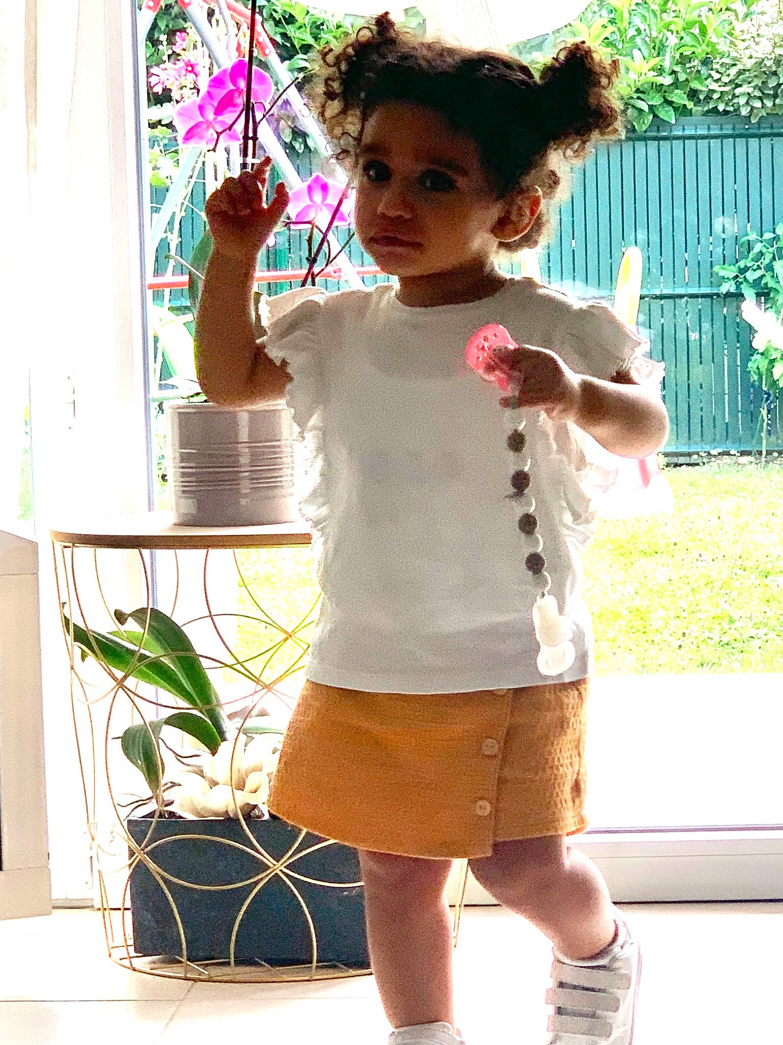 Myah participe au concours pour gagner de l'argent avec cette photo : baby_toddler_clothing, curtain, flowerpot, green, happy, houseplant, joint, knee, neck, person, plant, shorts, shoulder, sleeve, standing, t_shirt, thigh, toddler, trunk, vertebrate