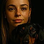 woman, dog, portrait, close_up, black_background, brown_eyes, black_dog, tan_markings, face, expression, pet, animal, human, indoor, looking_at_camera, female, mammal, companion, friendship, calm
