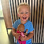 blonde_hair, blue_shirt, casual_clothing, child, cute, doll, face, happy, holding, indoor, joyful, person, pink_clothing, playful, short_hair, small_child, smiling, toddler, toy, wooden_slats