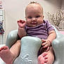 baby, barefoot, cheeks, child, cute, face, feet, flower_branch, foam_seat, furniture, hand_raised, indoor, infant, person, purple_onesie, room, seated, skin, smiling, television